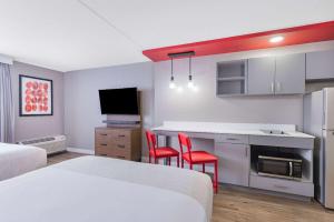 a hotel room with a bed and a kitchen with two red chairs at Hawthorn Extended Stay by Wyndham Wichita Airport in Wichita