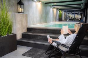 a woman sitting in a chair reading a book next to a swimming pool at Hotel Polonia PARK Medical Center & Spa in Busko-Zdrój