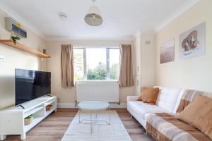uma sala de estar com um sofá branco e uma televisão em Lovely Studio Flat in Wimbledon w/ Free Parking em Londres