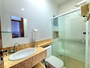 a bathroom with a sink and a toilet and a glass shower at Apartamento com piscina em UBATUBA in Ubatuba