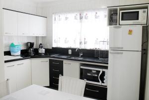 La cuisine est équipée de placards blancs et d'un réfrigérateur blanc. dans l'établissement Cantinho Aconchegante Morada do Sol, à Piratuba