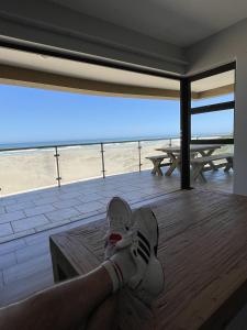 a person with their feet up on a table with a view of the beach at Paradise Beachfront Apartment in Jeffreys Bay