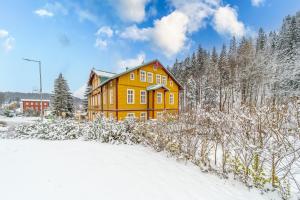 a yellow house in the snow with trees at Pension Janský Potok I. in Janske Lazne