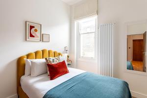 a bedroom with a bed with a yellow headboard and a window at Stunning Earls Court Flat in London