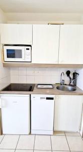 een witte keuken met een magnetron en een wastafel bij "SOLEIL DU GOLF" Appartement 5 personnes, vue golf, accès parc aquatique in Talmont