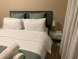 a bed with white sheets and green pillows next to a table at Sparrow Apartment in Johannesburg