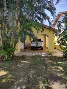 a car parked outside of a yellow house with palm trees at Casa com piscina em Bertioga in Bertioga