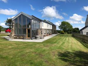 a house with glass doors and a grass field at The Barn at Ballaloaghtan in Ballasalla