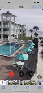 a swimming pool with tables and umbrellas next to the beach at Coastal Waters 209 in New Smyrna Beach