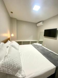 Un dormitorio con una cama blanca y un televisor de pantalla plana. en Casa Amora, en Arraial do Cabo