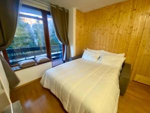een slaapkamer met een wit bed en een raam bij La Finestra sul Brenta con POSTO AUTO PRIVATO AL CENTRO di MAD di Campiglio CIPAT O22233-AT-O13262 in Folgarida