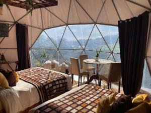 Habitación con una gran ventana de cristal con mesa y sillas. en Poas Volcano Observatory Lodge & Glamping en Poasito
