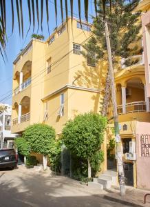 a yellow building with trees in front of it at Résidence SOTOUR, Liberté 6 Extension VDN - Newly Renovated Luxury 1 , 2, 3 and 4- Bedroom Apartment-Condos, Living Room, Kitchen and Balcony in Dakar