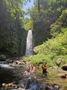three people swimming in a stream in front of a waterfall at Bunga Maliq Bungalow Lombok in Tetebatu