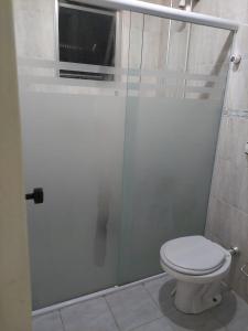 a bathroom with a toilet and a glass shower door at Cantinho de vó - Praia Grande - Aviação in Solemar