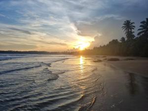 un coucher de soleil sur une plage avec la marée arrivant dans l'établissement Relax Beach House, à Tangalle