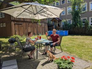 dwoje ludzi siedzących przy stole pod parasolką z psem w obiekcie Urlaubsmagie - Kleiner Wohlfühlort mit Pool - H4 w mieście Sebnitz