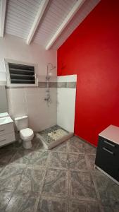 a bathroom with a toilet and a red wall at LE NID d'oiseau studio meublé climatisé chez l'habitant in Deshaies