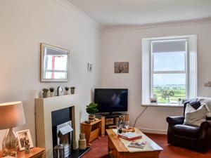 a living room with a tv and a chair and a table at Muirston Farmhouse in Ochiltree