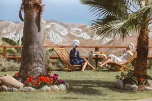 dos mujeres sentadas en sillas en una mesa en un jardín en Calàmi - Villa Romeo - Private Apartments with Pool, Seaview & Olive Grove, en Santa Caterina Dello Ionio Marina
