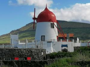 un molino de viento rojo y blanco con una colina al fondo en Moinho Mó da Praia, en Praia da Graciosa