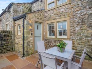 a patio with a table and chairs in front of a stone building at Graydon Cottage in Wigglesworth