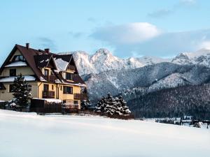 a house in the snow with mountains in the background at Panorama Premium in Kościelisko