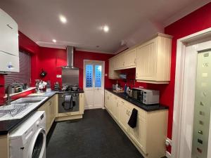 a large kitchen with red walls and white cabinets at Quebec House - Free Parking and Wifi, 'Comfortable Spacious House Near to Town Centre in Swindon