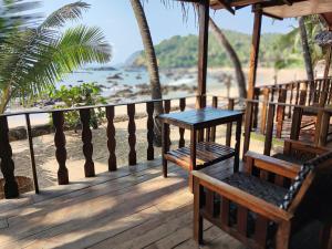 una terraza de madera con mesa y sillas en la playa en Sea Front Cottage Little Khola, en Cola