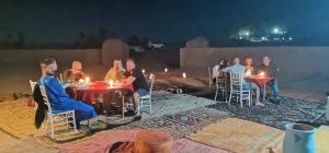 een groep mensen die rond een tafel met kaarsen zitten bij Camp M'hamid Ras N'khal in Mhamid