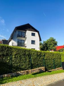 a white house with a black roof behind a hedge at MAWAROOMS in Świeradów-Zdrój