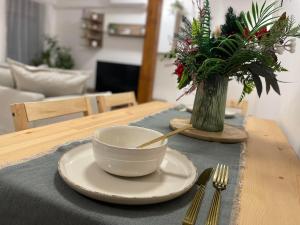 een tafel met een kom en vork en een vaas met bloemen bij Taverna Apartman in Monor