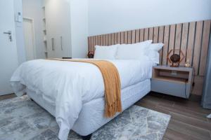 a bedroom with a large white bed with a wooden headboard at Luxe Lumiere @ The Habitat Alpha in Gaborone