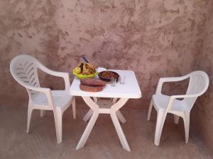 einen weißen Tisch mit einer Schüssel Essen und zwei Stühlen in der Unterkunft Ajgal imzi in Tiznit