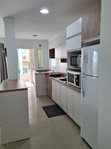 uma cozinha com armários brancos e um frigorífico branco em Amplo e aconchegante apartamento com 3 quartos a 50m da praia de Bombas em Bombinhas