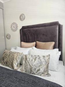 een bed met witte kussens en een bruin hoofdeinde bij Luxie@92 in Midrand