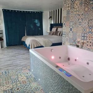 een badkamer met een bad en een slaapkamer met een bed bij L’Appar(T) du Grand Bois - Jacuzzi - in Soucelles