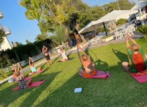 eine Gruppe von Kindern, die Yoga im Gras machen in der Unterkunft Villaggio Poseidone Beach Resort - Hotel in Torre San Giovanni Ugento
