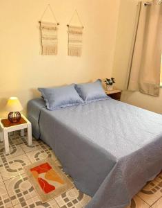um quarto com uma cama com lençóis azuis e uma mesa em No Centro a 3 min da praia, Pet Friendly e Wi Fi em Peruíbe