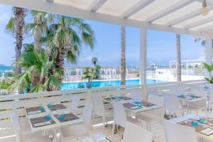 a restaurant with white tables and chairs and a swimming pool at Villaggio Poseidone Beach Resort - Hotel in Torre San Giovanni Ugento