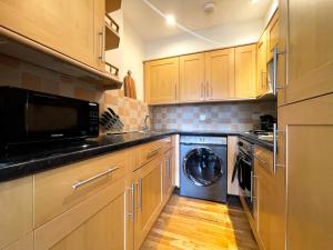 uma cozinha com armários de madeira e uma máquina de lavar e secar roupa em Camden Elegance : Cozy&Modern (10 min to center) em Londres