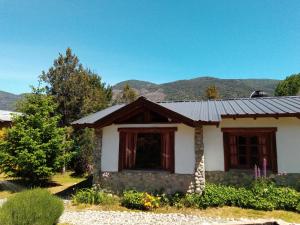 una pequeña casa blanca con montañas en el fondo en Cabañas Aldea de Montaña en Lago Puelo