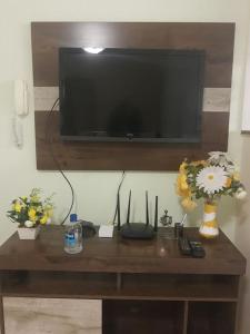 uma mesa de madeira com flores e uma televisão na parede em Apto Edifício Esmeralda em Viçosa