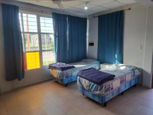 two beds in a room with blue curtains and a window at Depto monoambiente temporario in Resistencia