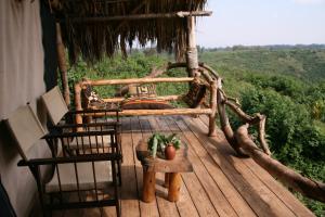 een veranda met stoelen en een bed op een houten terras bij Crater Forest Tented Lodge in Karatu