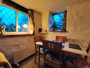 a dining room with a table and chairs and two windows at Yr Hen Efail - Quirky Old Smithy cottage near forest walks, cycling & lakes in Garthbeibio