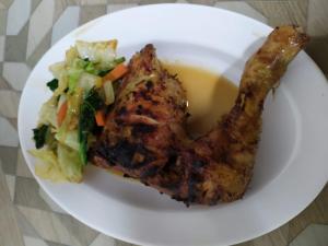 a white plate with a piece of meat and a salad at Baruna Cottages in Kintamani