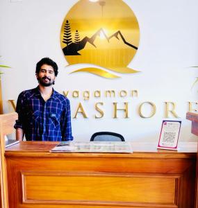 a man standing behind a desk in front of a sign at Vagamon Vagashore in Vagamon