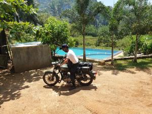 un homme assis sur une moto à côté d'une piscine dans l'établissement Sinharaja Hostel, à Deniyaya