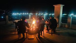 een groep mensen die 's nachts rond een vuurplaats zitten bij Hotel The Meadows Open Terrace Bonfire in Manāli